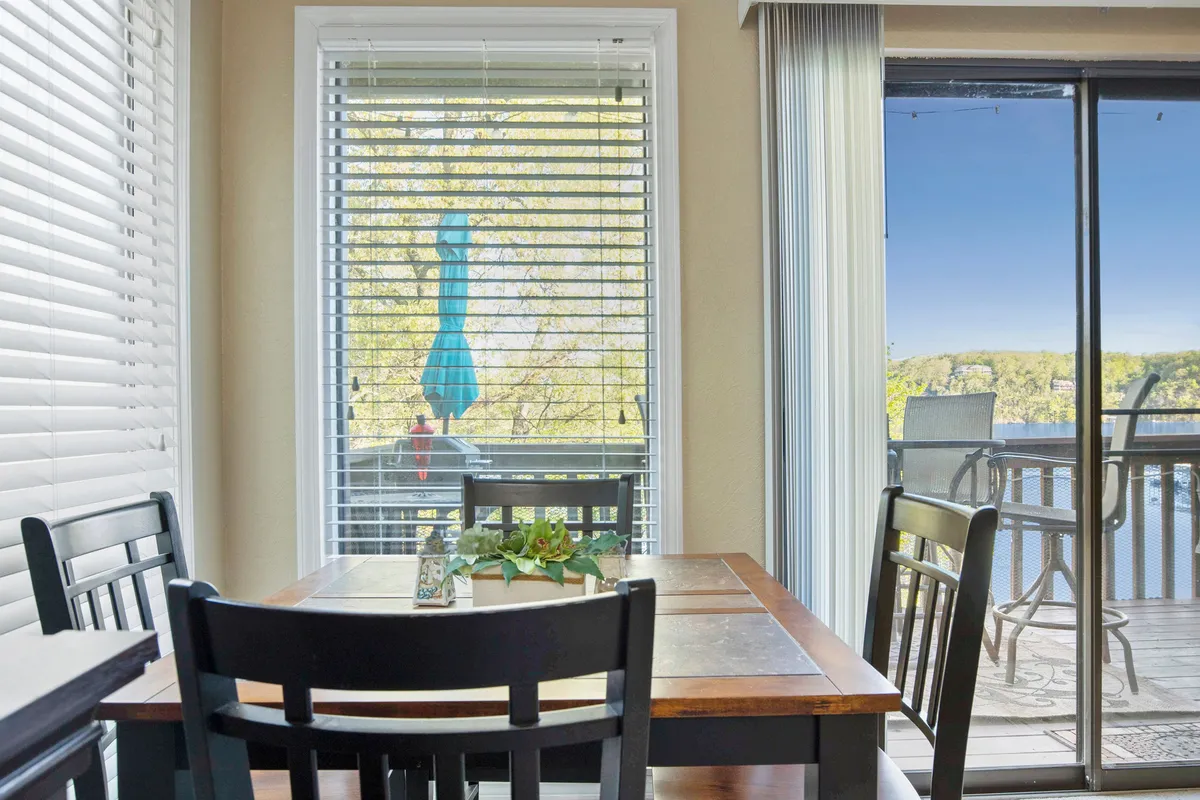 A serene dining nook featuring a small dining table set by a window with blinds, allowing for tranquil glimpses of the balcony and outdoors. A decorative plant adds a fresh touch. The intimate setting is ideal for family breakfasts or romantic dinners as described in the section.