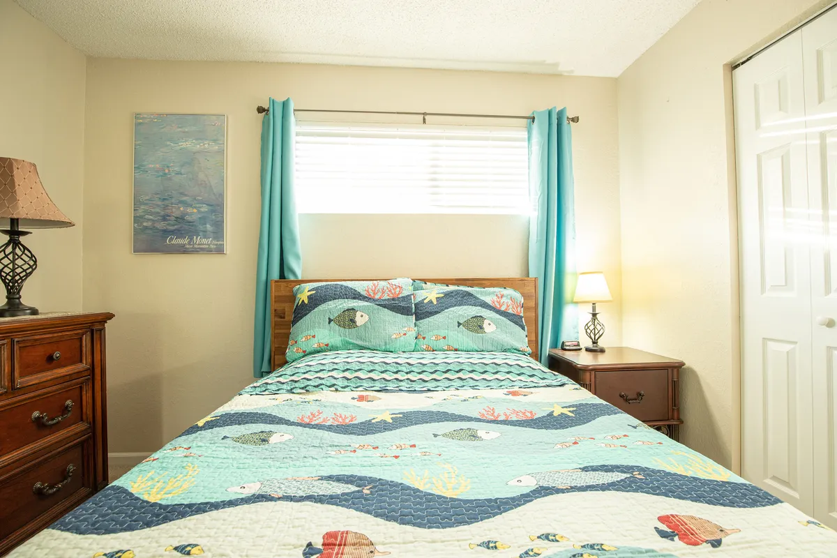 A peaceful bedroom scene with a bed covered in a vibrant quilt, a nightstand softly illuminated by a lamp, and tasteful wall art. The space feels welcoming and restful, ideal for winding down after a busy day.