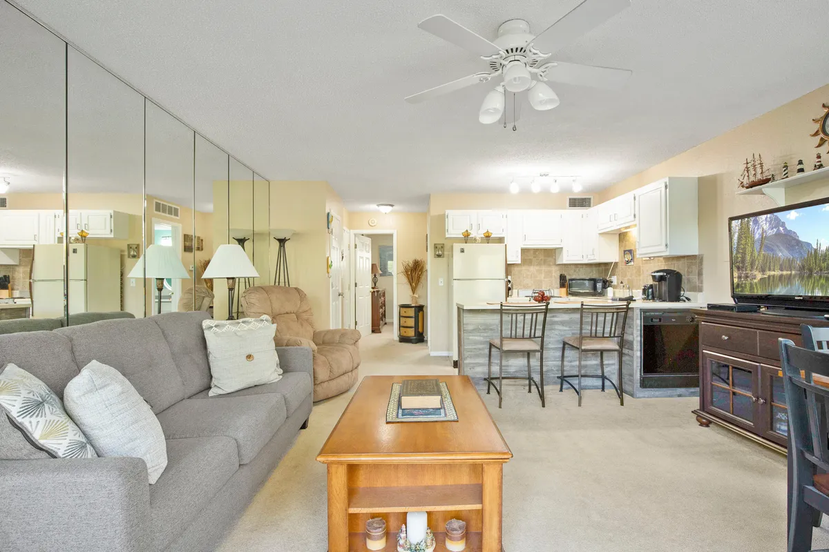 A warm, inviting living area featuring a plush sofa, coffee table, kitchen space, and mirrored wall, ideal for sharing coffee, unwinding after a day of exploring, or planning a cozy night in.