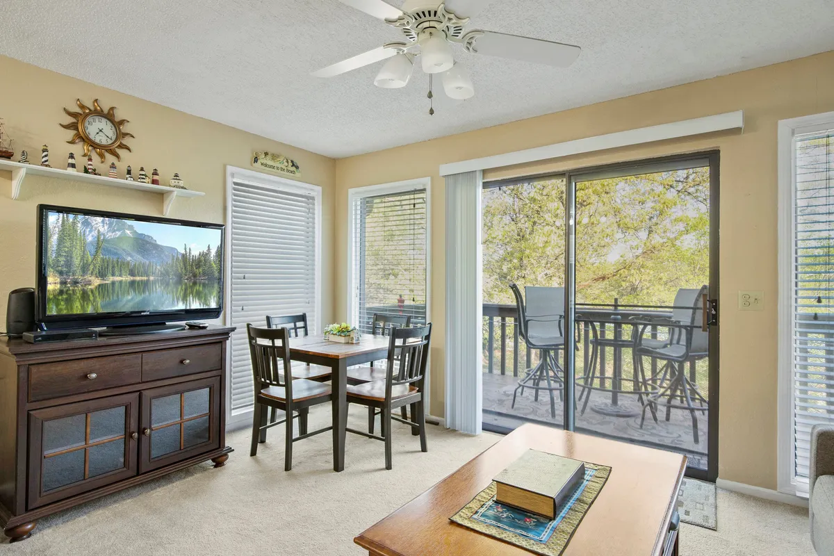 An interior dining area with a cozy table set near a large sliding glass door, offering views onto a balcony. The setup is ideal for shared meals, playing games, or enjoying a movie together while still visually connecting to the outdoors.
