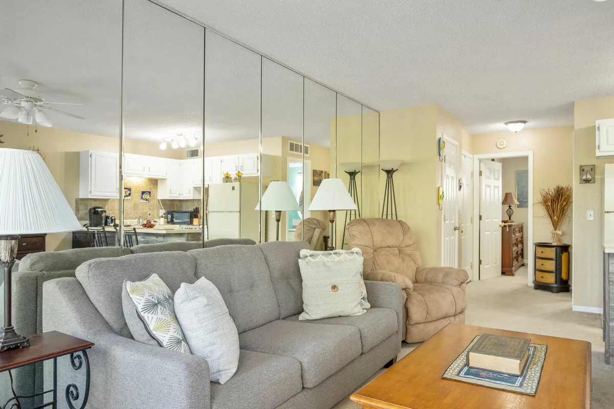 A cozy living room featuring a gray sofa, a wood coffee table, a mirrored wall reflecting more of the space, and a comfortable armchair. The setup is perfect for relaxing, socializing, or spending a quiet afternoon inside after a day of adventure.
