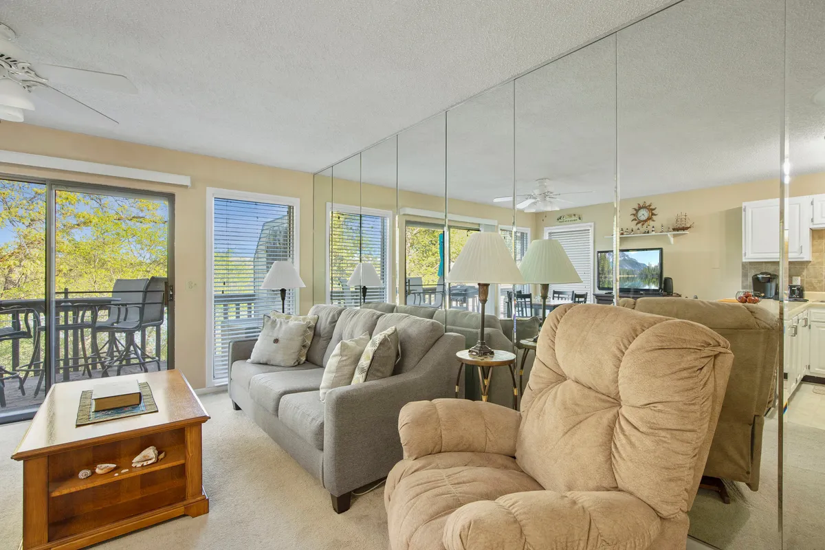 A cozy living room setup featuring a plush sofa, recliner, and coffee table positioned in front of large windows. The windows lead out to a balcony and capture beautiful sunset light, inviting guests to relax and enjoy the view.